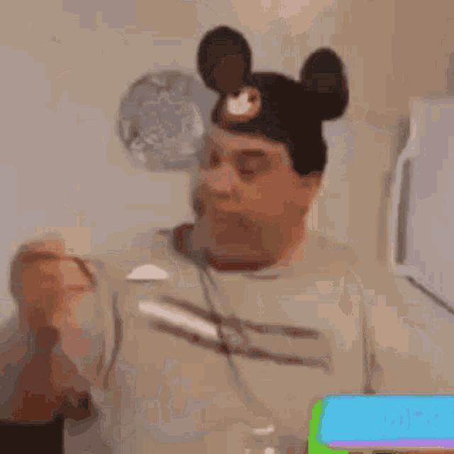 a man wearing a mickey mouse hat is eating a bottle of ice cream .