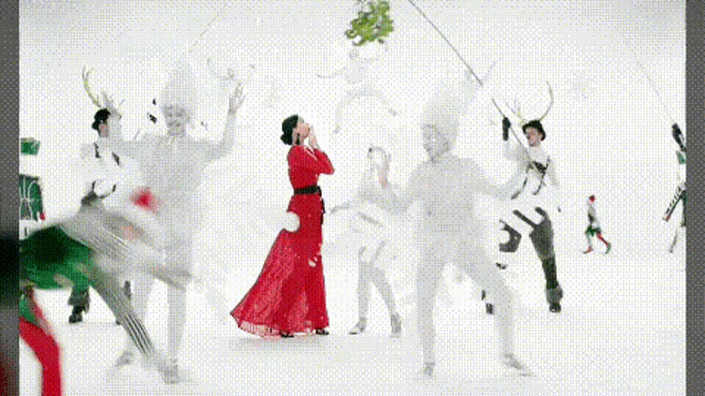 a woman in a red dress is surrounded by a group of white people holding mistletoe .