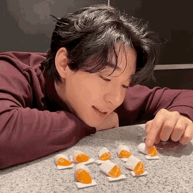 a man in a maroon sweatshirt is laying on a counter with a bunch of orange slices on it