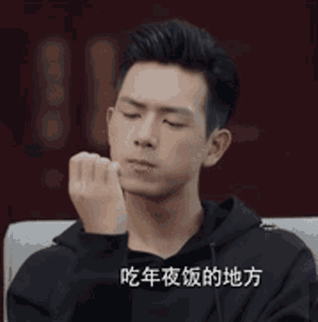 a man in a black hoodie is sitting on a couch with his hand to his face .
