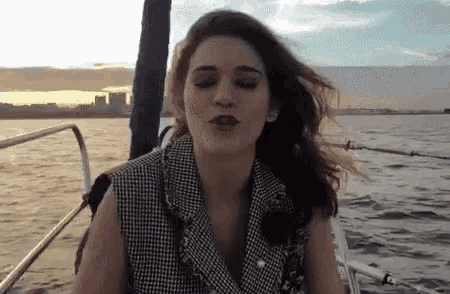 a woman is blowing a kiss while sitting on a boat in the water .