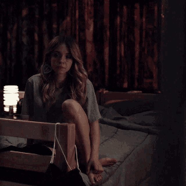 a woman is sitting on a bed with her legs crossed and a bag hanging from her feet