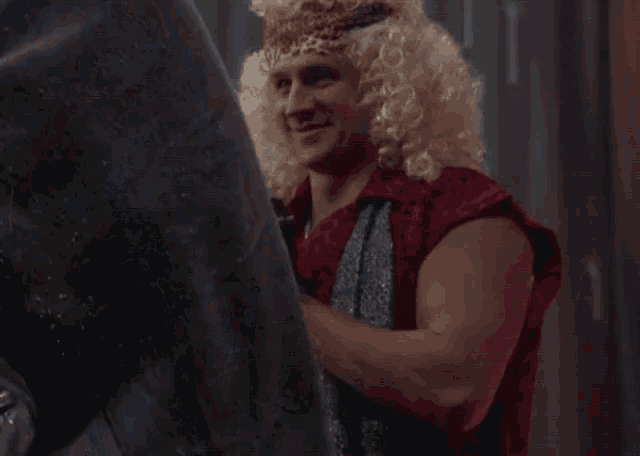 a man wearing a wig and a crown is standing in a dark room