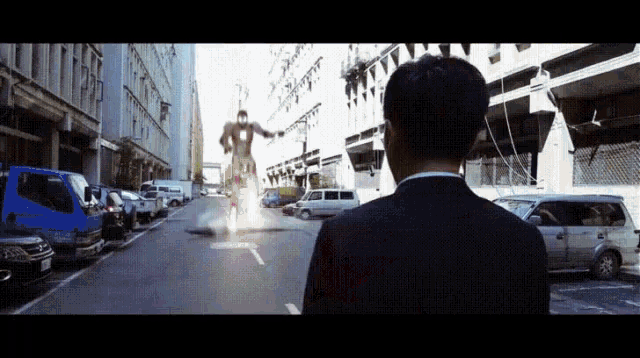 a man in a suit stands on a street looking at a giant robot