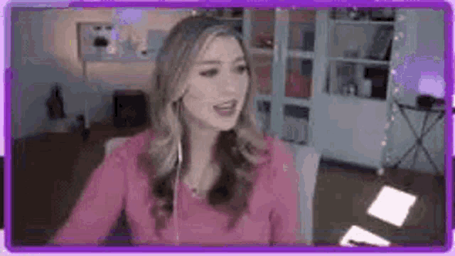 a woman in a pink shirt and headphones is sitting at a desk in a living room .
