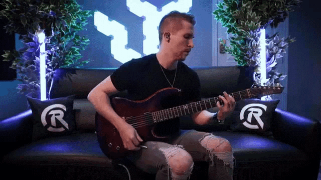 a man is playing a guitar on a couch with pillows that say r on them