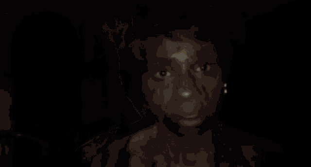 a woman with blood on her face looks at the camera in a dark room