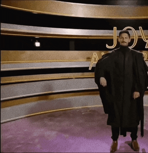 a man in a black cape is standing in front of a wall that says joy