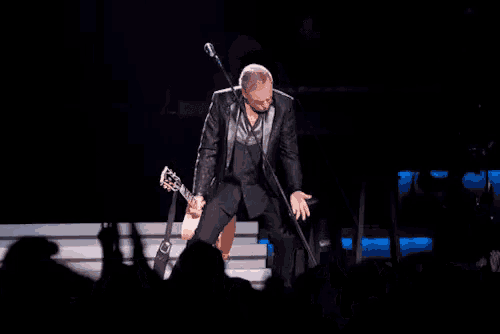 a man holding a guitar and singing into a microphone on a stage