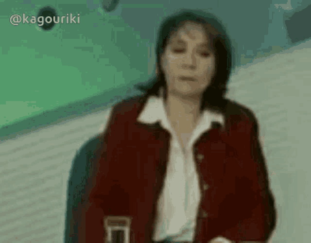 a woman in a red jacket is sitting in front of a green background .