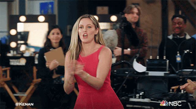 a woman in a red dress stands in front of a group of people and a sign that says nbc