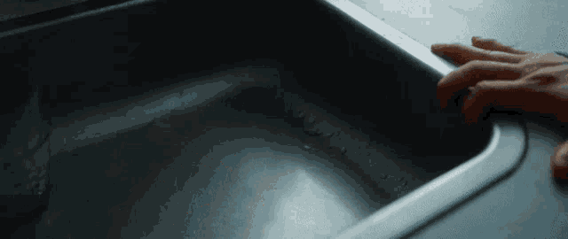 a person 's hand is reaching into a sink filled with water
