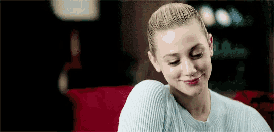 a woman in a blue sweater is sitting on a couch smiling .