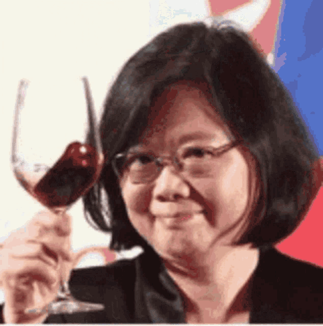 a woman with glasses is holding a glass of red wine .