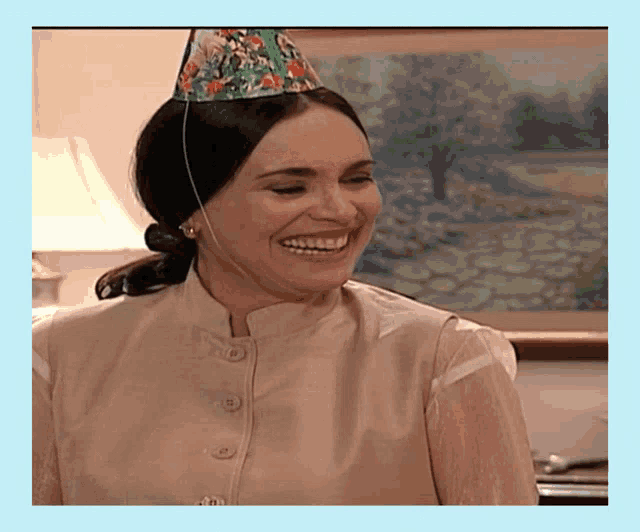 a woman wearing a party hat is smiling in front of a picture