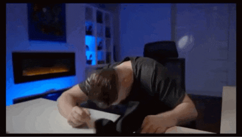 a man is laying down at a desk with his head on the table .