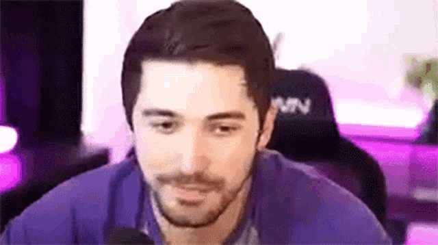 a man with a beard is sitting in front of a microphone in a purple chair .