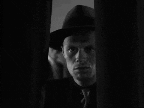 a man in a fedora looks out a window in a black and white photo