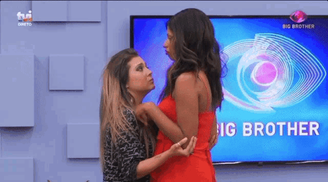 two women are standing in front of a big brother tv screen