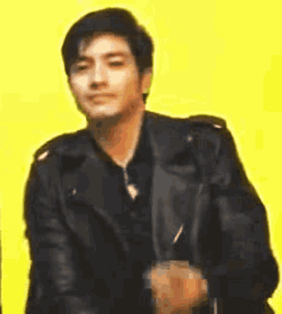 a man wearing a black leather jacket is dancing on a yellow background .