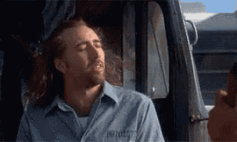 a man in a blue shirt is sitting in a truck smoking a cigarette .