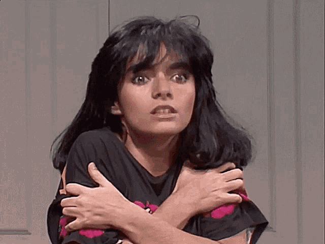 a woman wearing a black shirt with red hearts on it is holding her arms around her chest