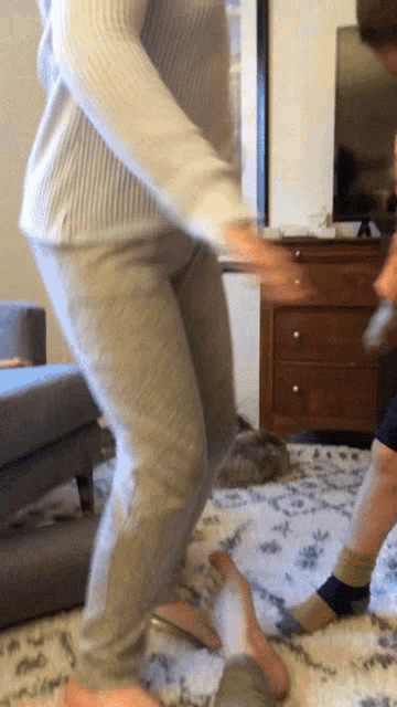 a woman in grey sweatpants is jumping in the air in a living room