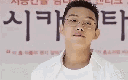 a man wearing glasses and a white shirt is standing in front of a sign in a room .