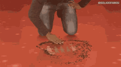 a man is kneeling down and drawing a heart with his hands on a red surface .