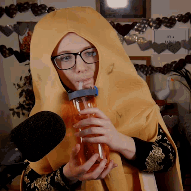 a woman wearing glasses and a yellow cape drinking from a bottle