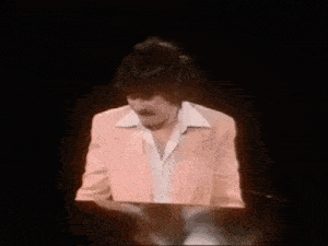 a man with a mustache is playing a piano in a pink suit .