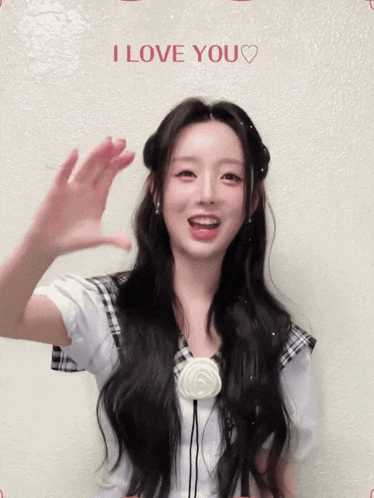 a woman waves her hand in front of a white wall that says i love you