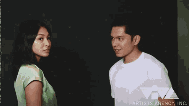 a man and a woman are standing next to each other and the artists agency inc. logo can be seen in the corner