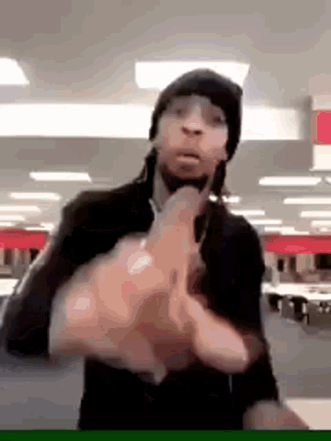 a man wearing a hat and glasses is giving the middle finger in a room .