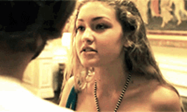 a woman wearing a necklace looks at a man in a room