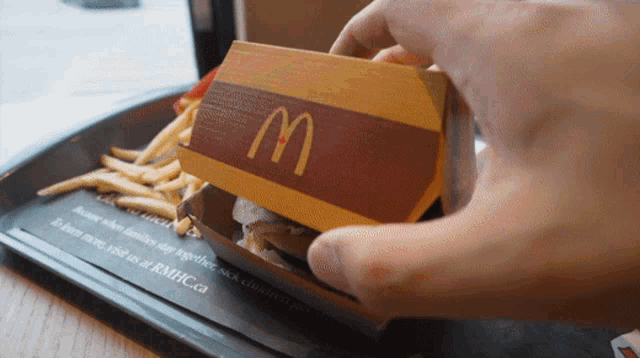 a person is opening a mcdonald 's box with french fries on the side