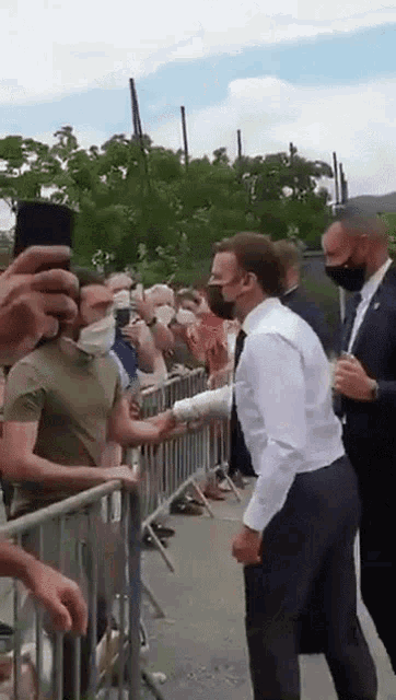 a man in a white shirt is standing in front of a crowd of people wearing masks .