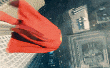 a man in a red cape is flying through the air over a city