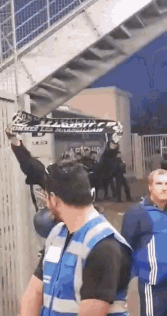 a man in a blue vest holds up a black and white scarf that says ' l' avenir ' on it