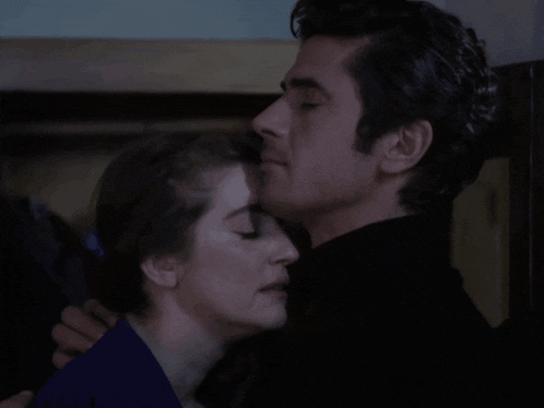 a man and a woman are hugging each other in a dark room with their eyes closed