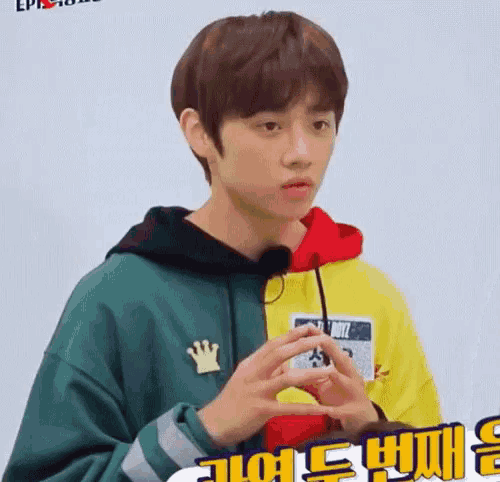 a young man wearing a green hoodie and a yellow hoodie is making a funny face .