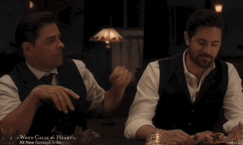 two men sitting at a table with a sign that says when calls the heart on it