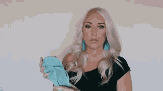 a woman with blonde hair and blue earrings is holding a blue cloth in her hands .