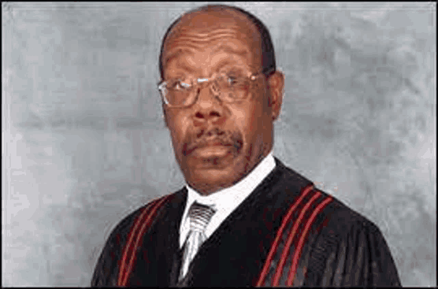 a man wearing a graduation gown and tie is standing in front of a wall .