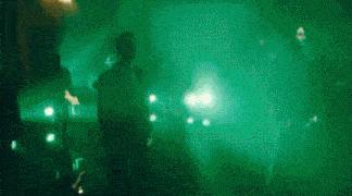 a group of people are dancing in a dark room with green lights and smoke .