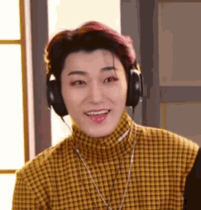 a young man wearing headphones and a plaid shirt is smiling .