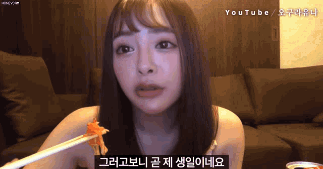 a woman is eating a piece of food with chopsticks with a youtube logo in the background