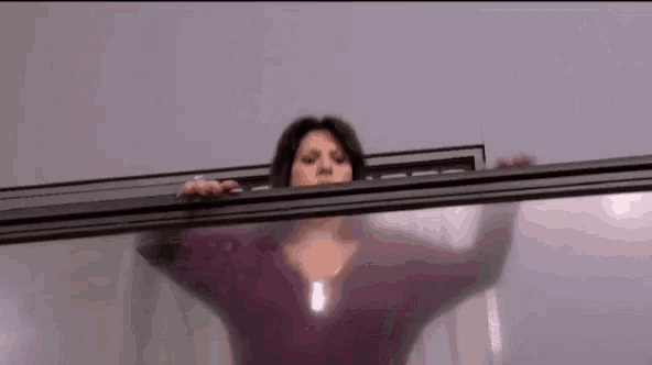 a woman is standing behind a glass wall looking out .