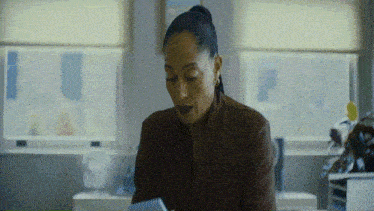 a woman in a brown shirt is sitting in front of a window looking at a tablet .