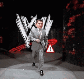 a man in a suit and tie is walking on a stage in front of a wwe logo